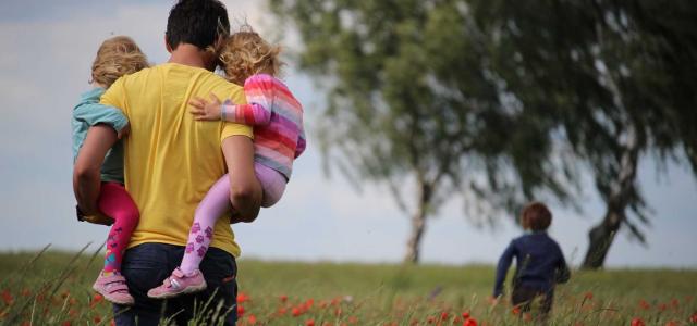 Dad holding children in field.